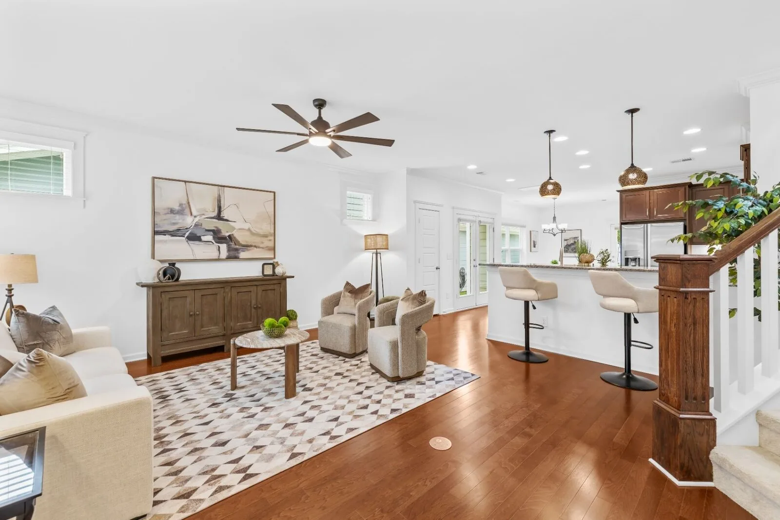 Staged living room interior with lounge seating, a kitchen island, and wood floors.