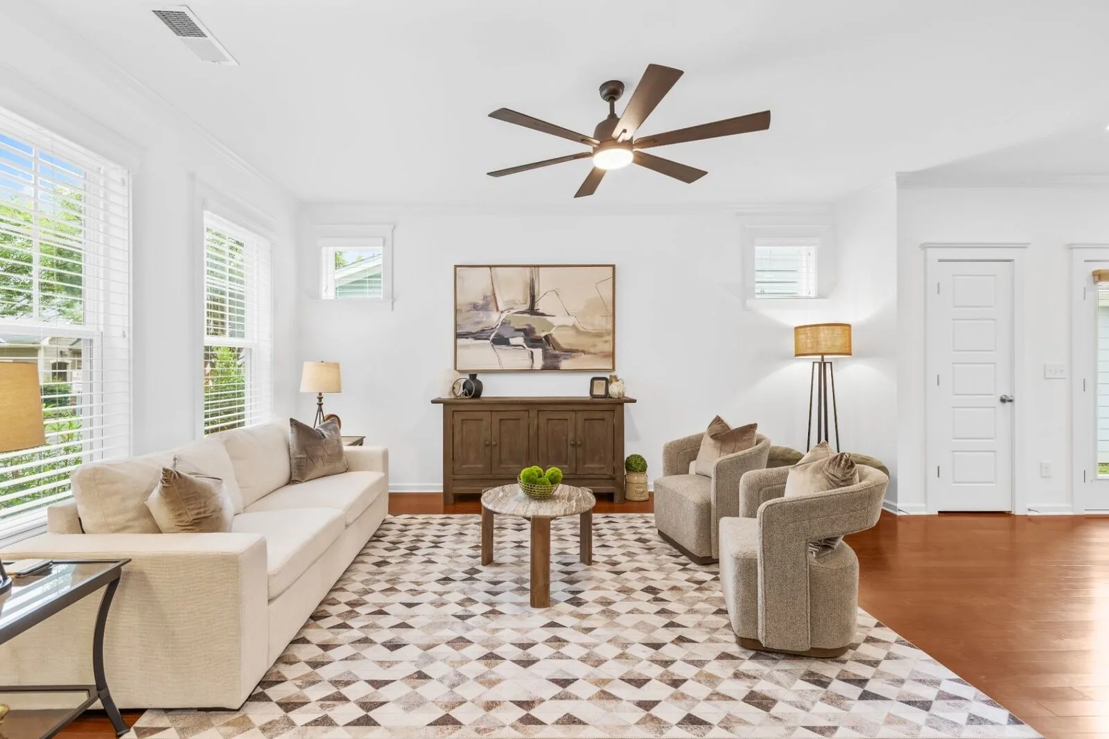 Staged living room interior with a light sofa, lounge chairs, a patterned rug, and wood floors.