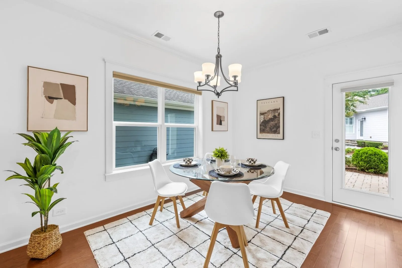 Dining area styling with a round glass table, white chairs, artwork, and a large window.