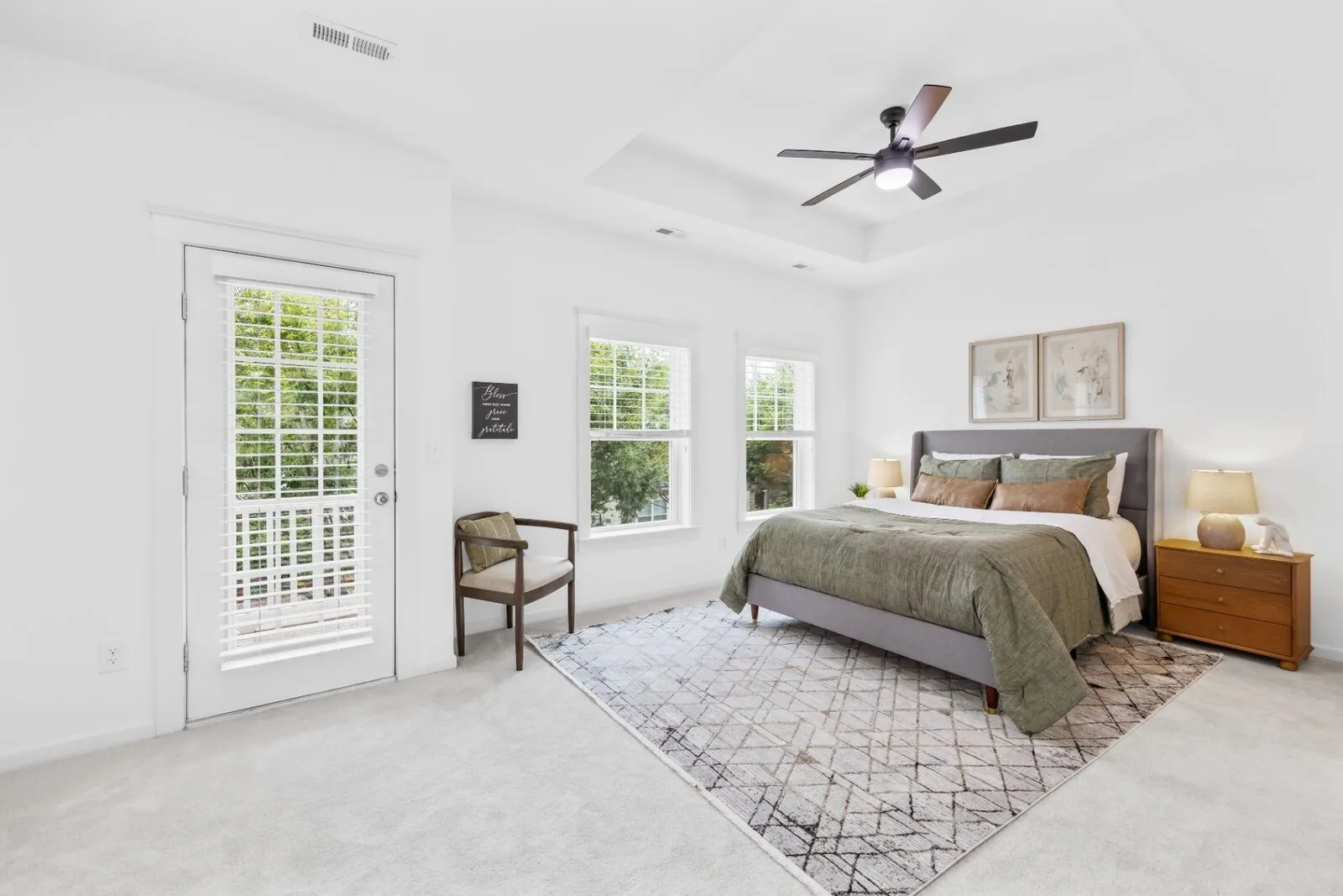 Curated bedroom interior with a gray upholstered bed, layered bedding, windows, and a patterned rug.