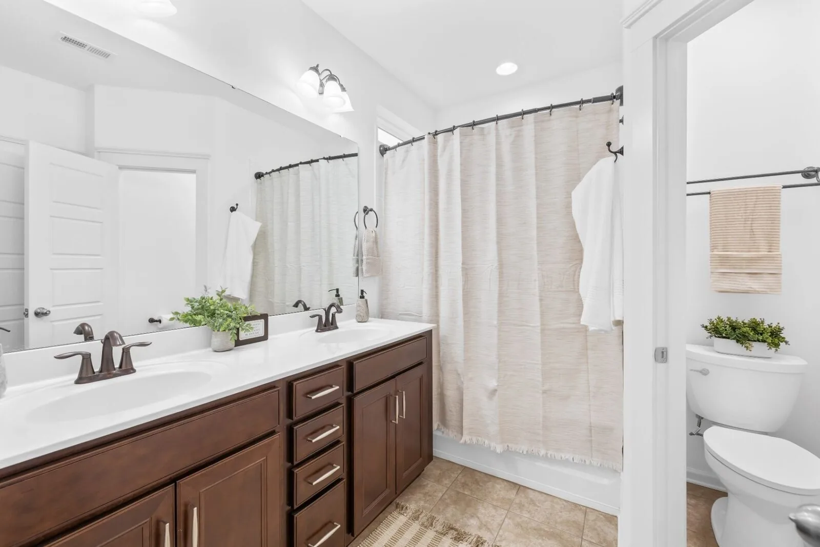 Bathroom styling with a double vanity, wood cabinetry, a large mirror, and a light shower curtain.