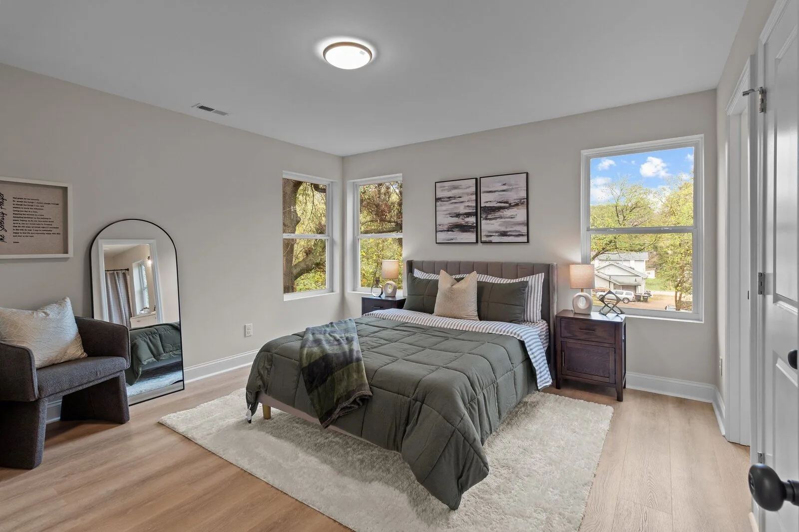 Curated bedroom interior with a light upholstered bed, layered white bedding, and green accents.