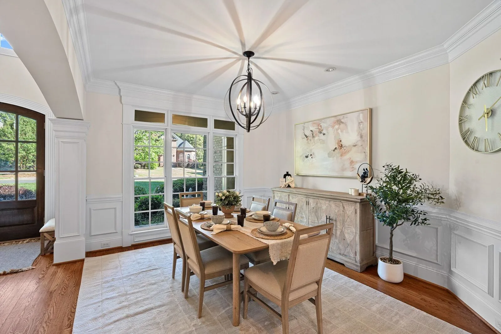Staged dining room with a wood table, upholstered chairs, artwork, and a sideboard.